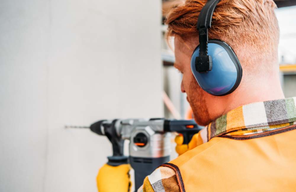 Worker wearing earmuffs for noise safety in a loud workplace, promoting HSEQ compliance and vocational training best practices.