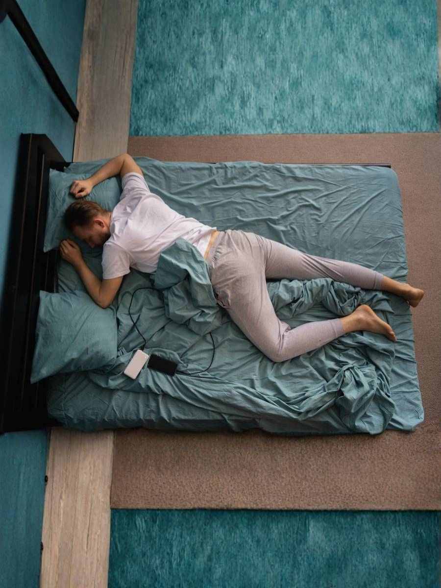 Man asleep on bed with phone and power bank charging beside him, illustrating the fire risks of overnight charging and unsafe device use.