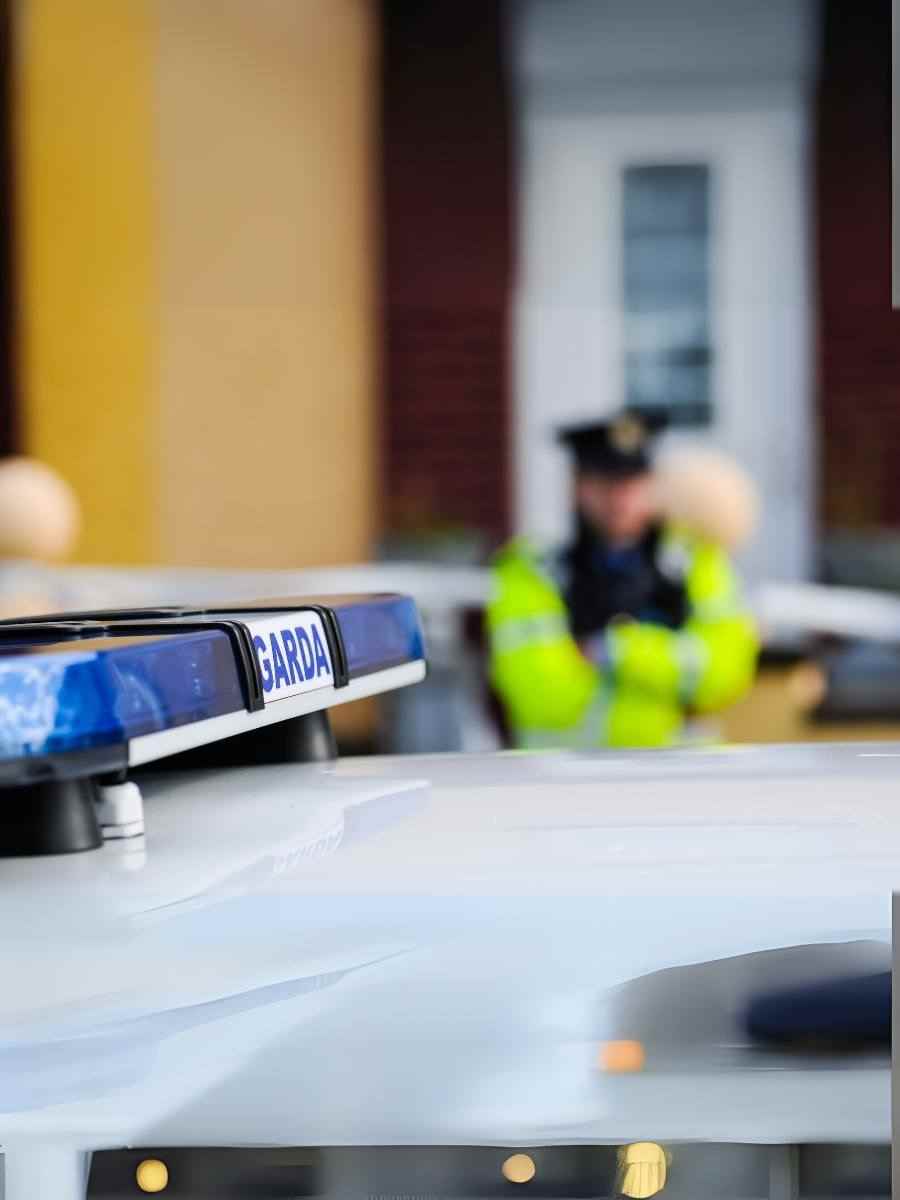 Garda emergency vehicle with blue light and blurred officer in high-visibility jacket in the background, representing Ireland’s investment in reliable communication systems for safety.